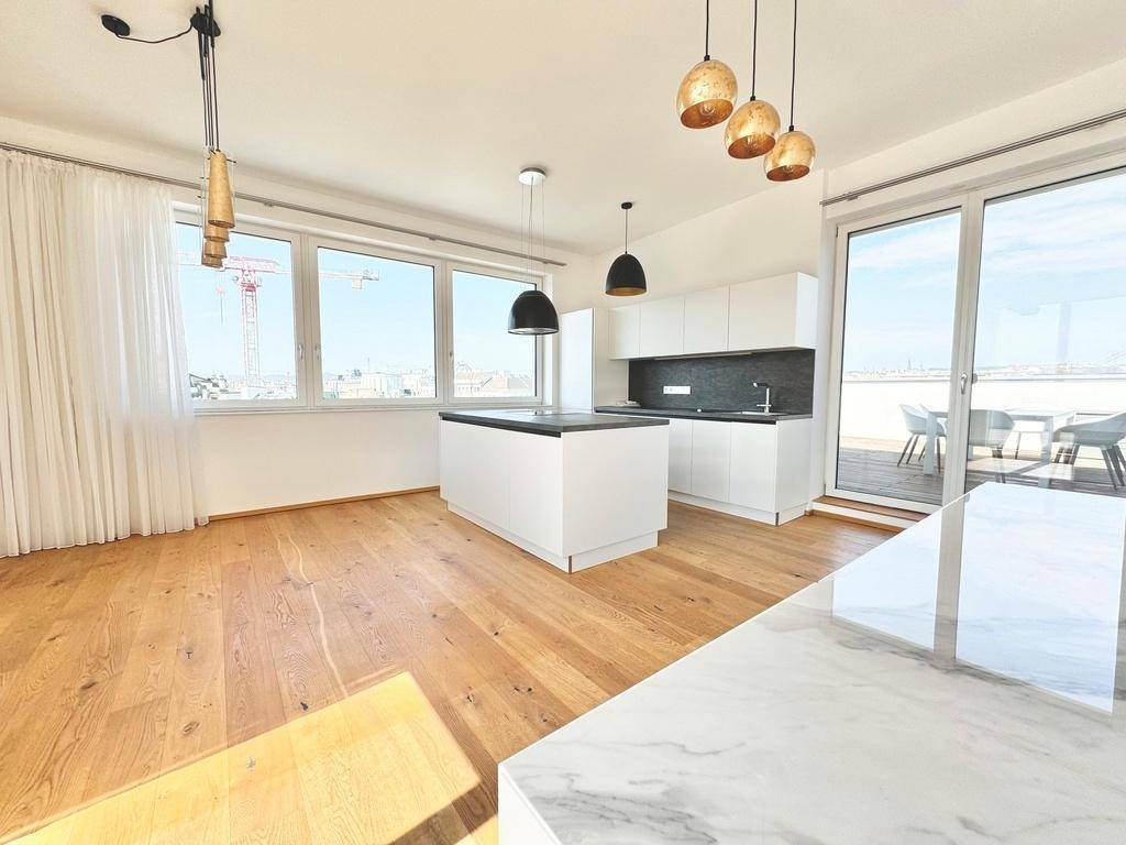 Heller offener Wohnbereich mit moderner weißer Küche, Kücheninsel und Zugang zur Terrasse durch große Fenster.