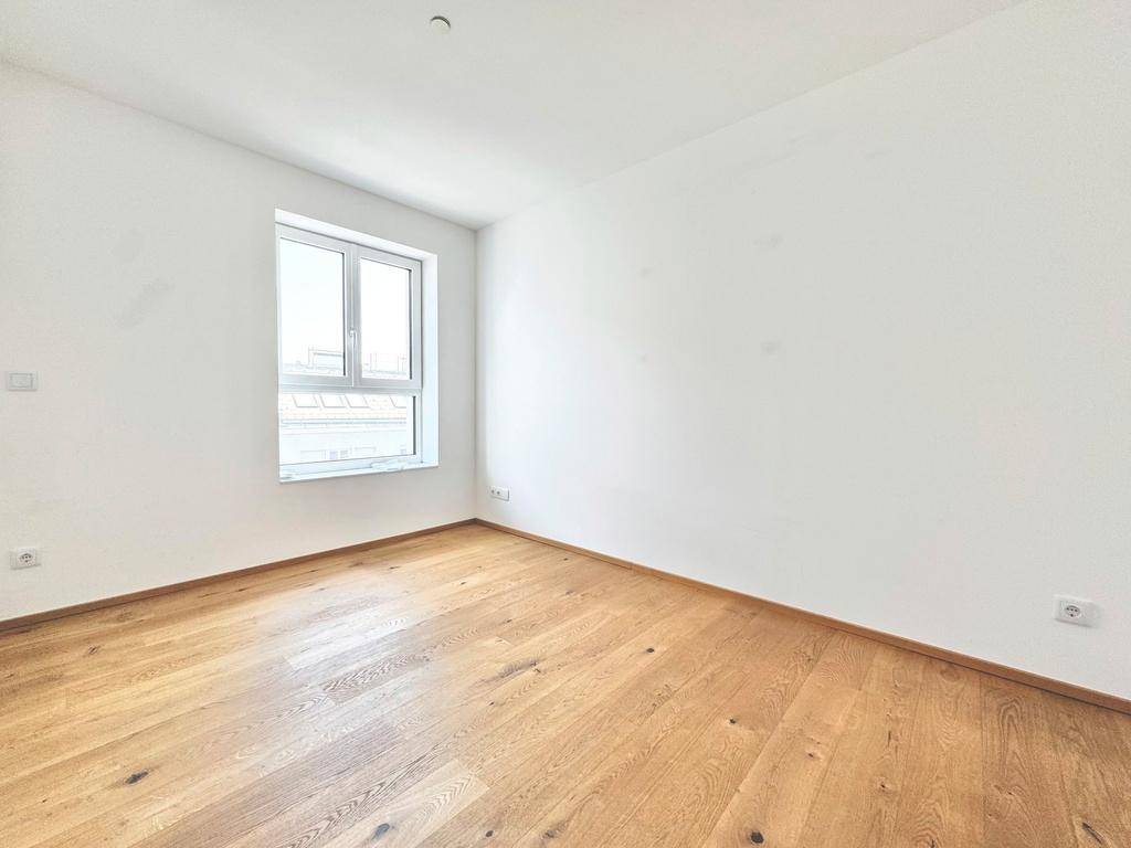 Helles, leeres Zimmer mit Holzboden und einem Fenster, das viel Tageslicht in den Raum bringt.