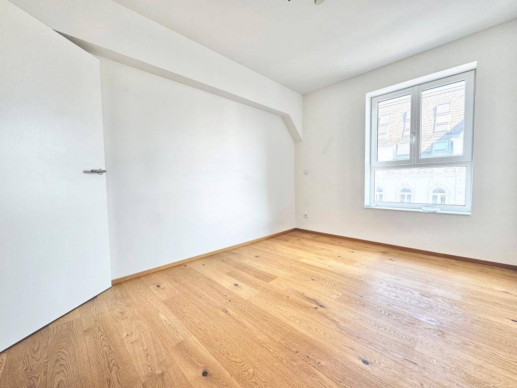 Leeres Zimmer mit weißen Wänden, Holzboden und einem Fenster, bereit zur individuellen Gestaltung.