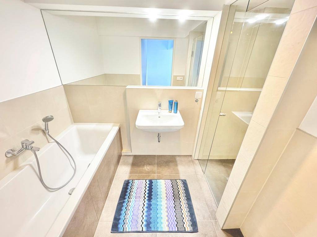 Modernes Badezimmer mit Badewanne, Einzelwaschbecken und begehbarer Dusche, hell gefliest.