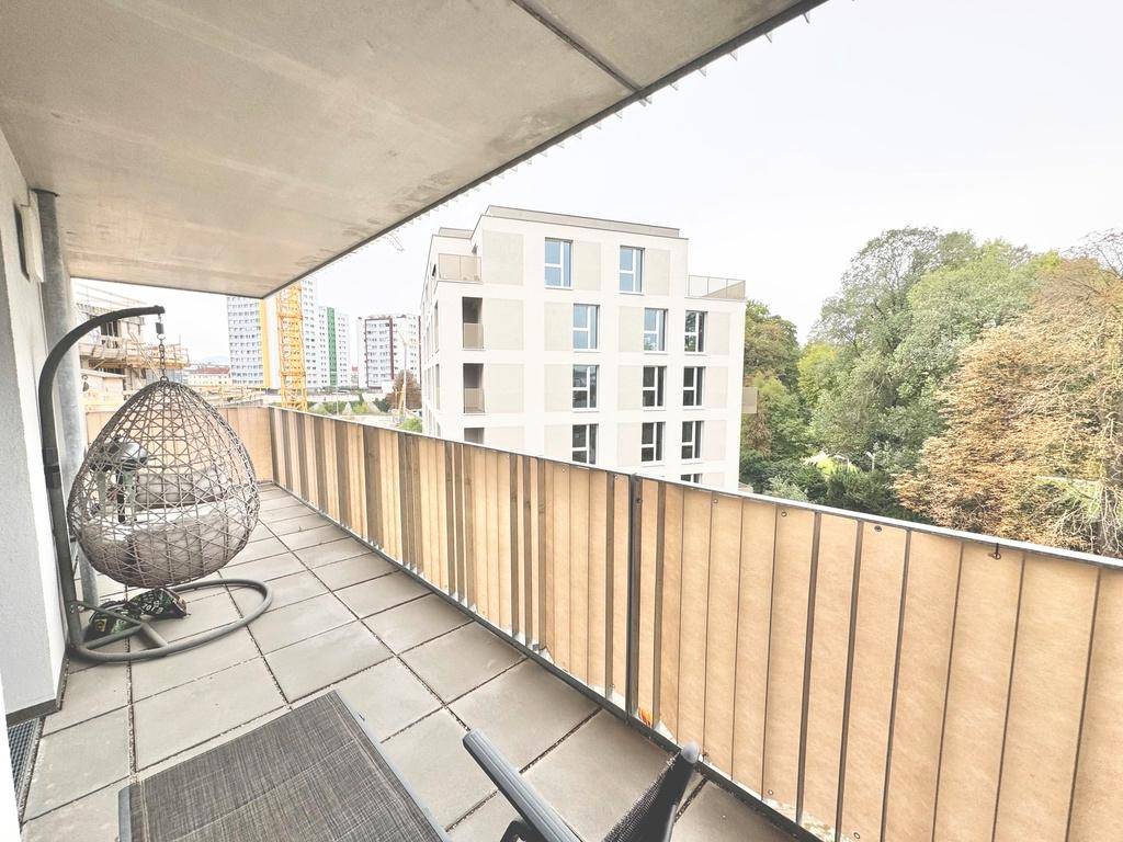 Geräumiger Balkon mit Hängesessel und Blick auf umliegende Gebäude und Bäume.