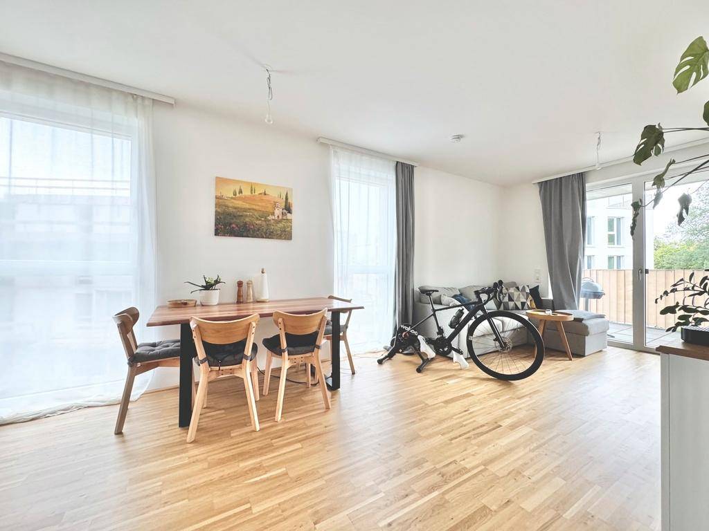 Offener Wohn-Essbereich mit Holztisch, Parkettboden und Zugang zum Balkon.