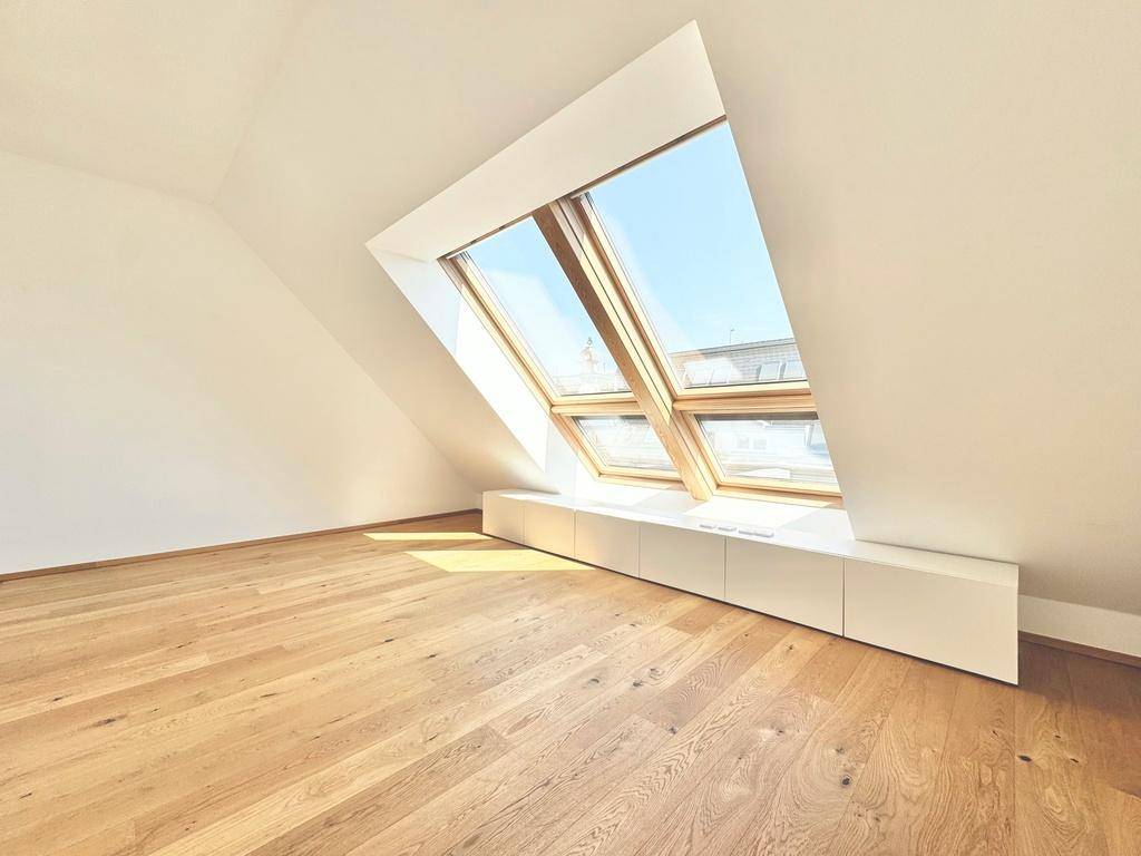 Heller Dachraum mit schrägen Decken, Holzboden und großen Dachfenstern, die viel Tageslicht hereinlassen.