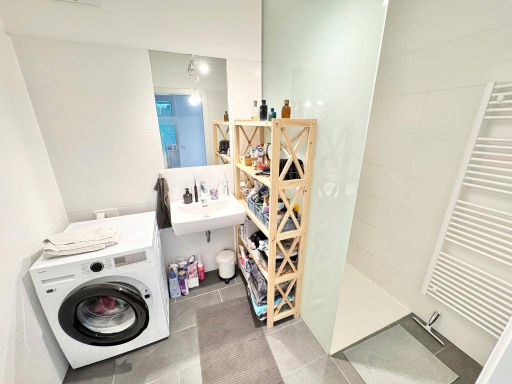 Modernes Badezimmer mit Dusche, Waschbecken, Waschmaschine und Handtuchheizkörper.