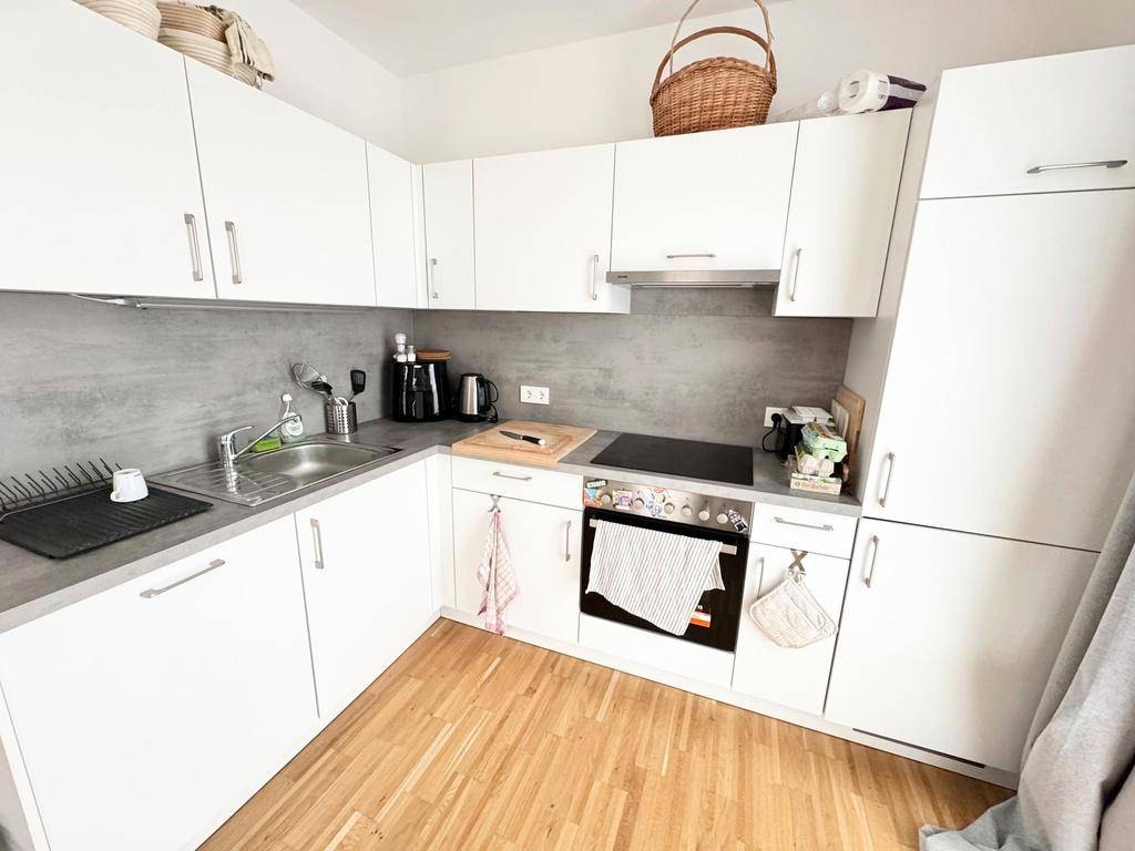 Moderne Einbauküche mit weißen Schränken, grauer Arbeitsplatte und Holzfußboden.