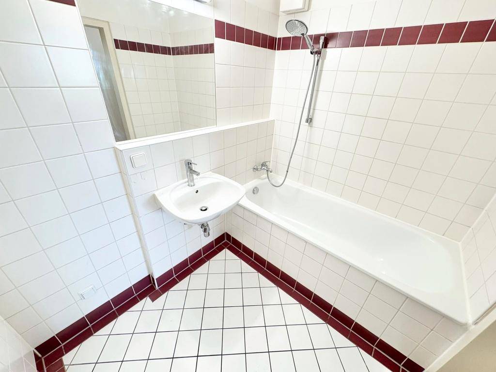 Gefliestes Badezimmer mit Badewanne, Waschbecken und roten Akzentstreifen.