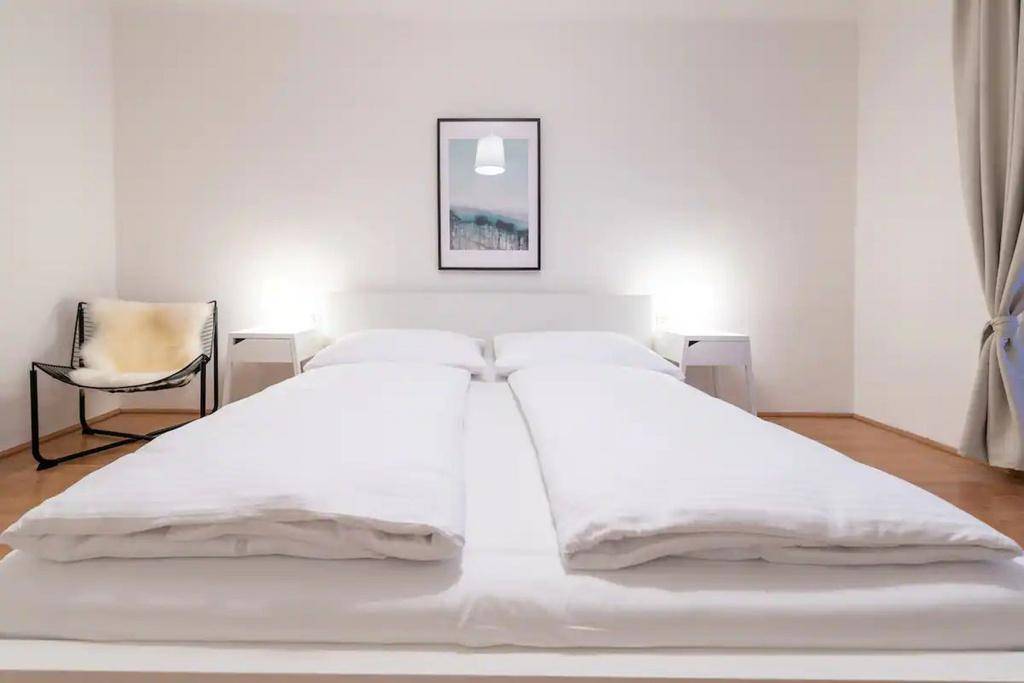 Komfortables Doppelbett mit weißen Bezügen und Nachttischen in einem hellen Schlafzimmer.
