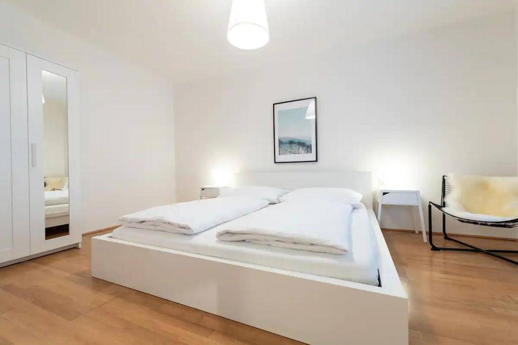 Modernes Schlafzimmer mit weißem Doppelbett, Spiegelschrank und Holzboden.