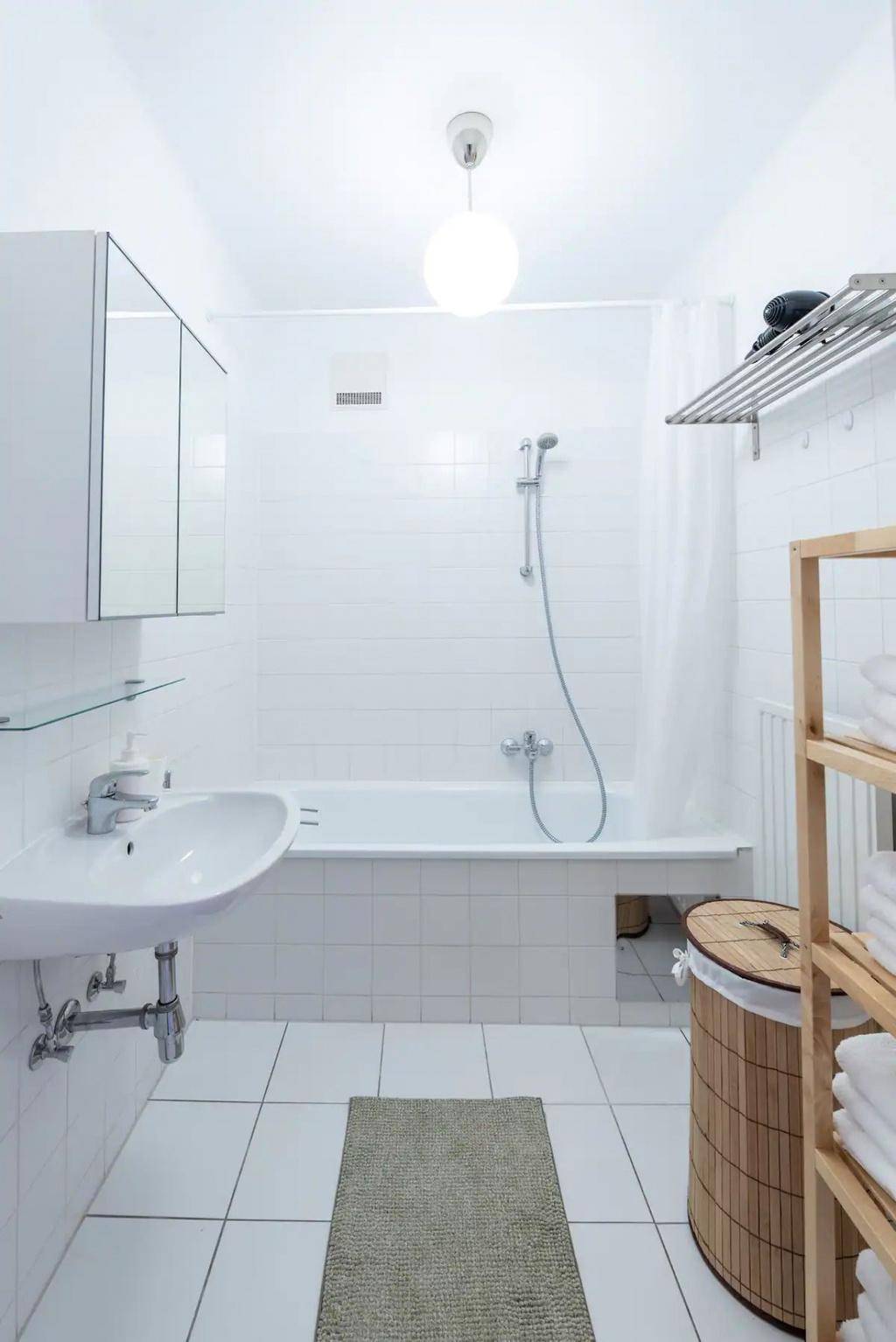 Weiß gefliestes Badezimmer mit Badewanne, Waschbecken und Spiegelschrank.