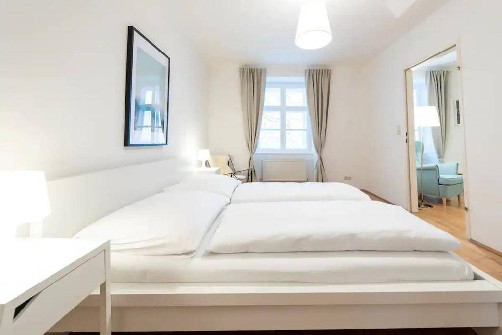 Helles Schlafzimmer mit weißem Bett, Fenster und Blick in den angrenzenden Wohnbereich.