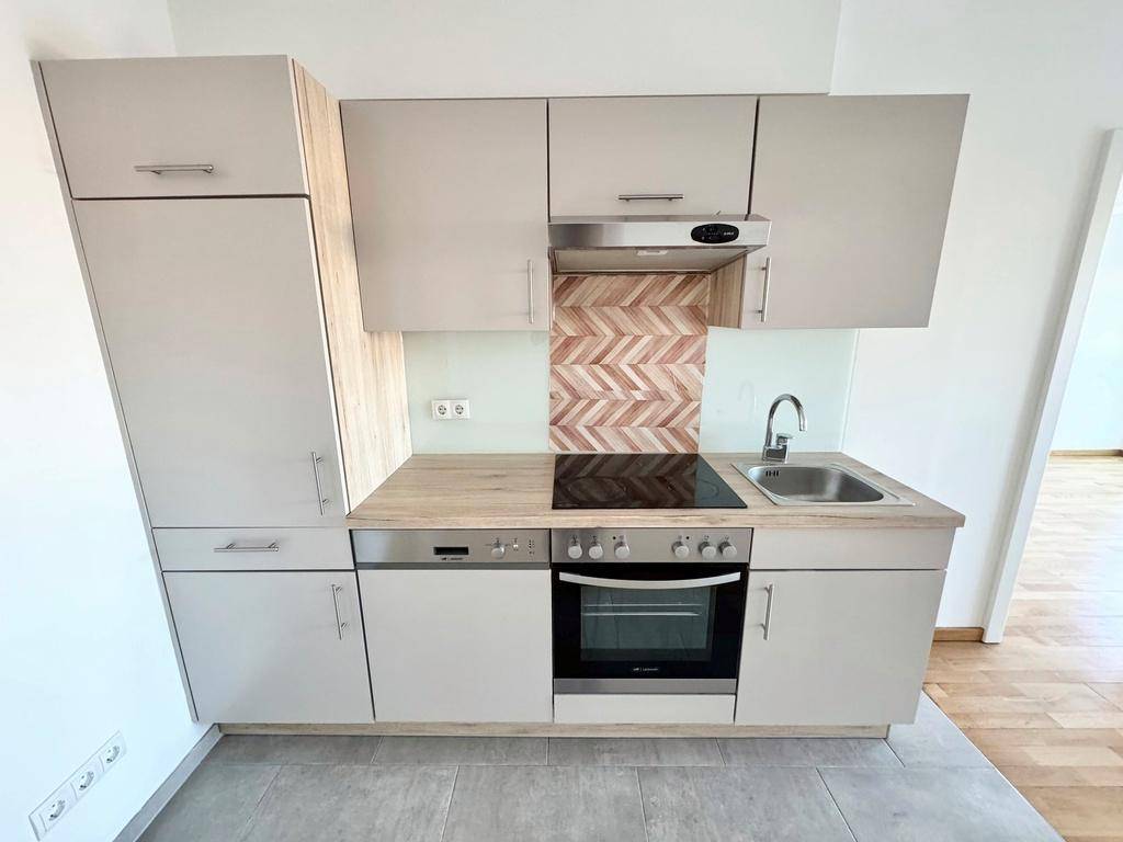 Moderne Küchenzeile mit hellen Schränken, Holz-Arbeitsplatte und integrierten Elektrogeräten.