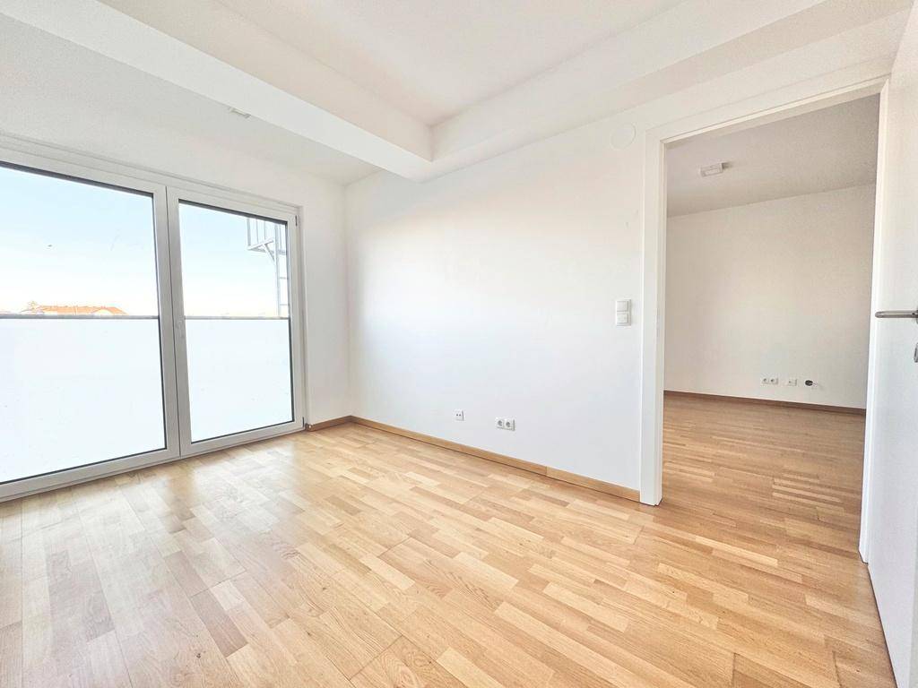 Helles Schlafzimmer mit Parkettboden und großem Fenster, das Zugang zu einem Außenbereich bietet.