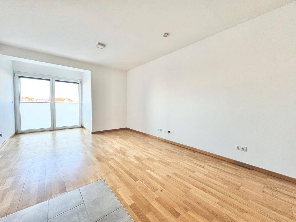 Geräumiger, heller Wohnbereich mit Parkettboden und großen Fenstern, die viel Tageslicht hereinlassen.