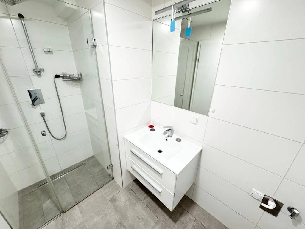 Modernes Badezimmer mit weißen Fliesen, ebenerdiger Dusche und schwebendem Waschtisch.