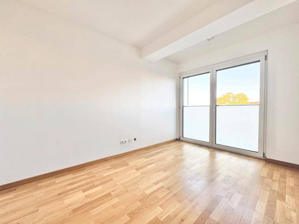 Lichtdurchfluteter Raum mit Holzboden und breiter Fensterfront, ideal als Schlaf- oder Arbeitszimmer.
