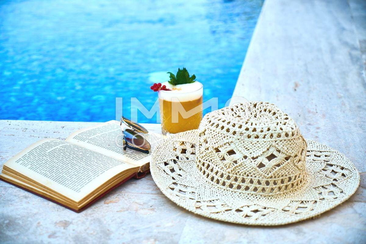 Symbolfoto Buch und Hut am Pool