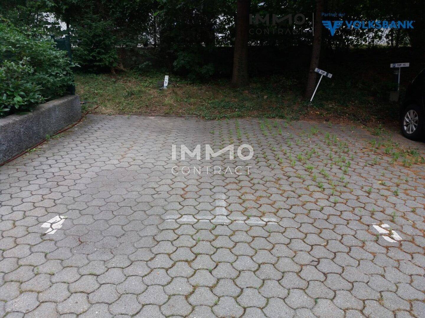 Gepflasterter Außenparkplatz mit Markierungen und umgebender Vegetation.