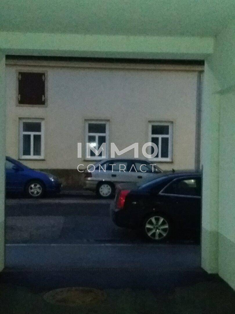 Blick durch einen Durchgang auf eine Straße mit geparkten Autos und einer gegenüberliegenden Gebäudefassade.