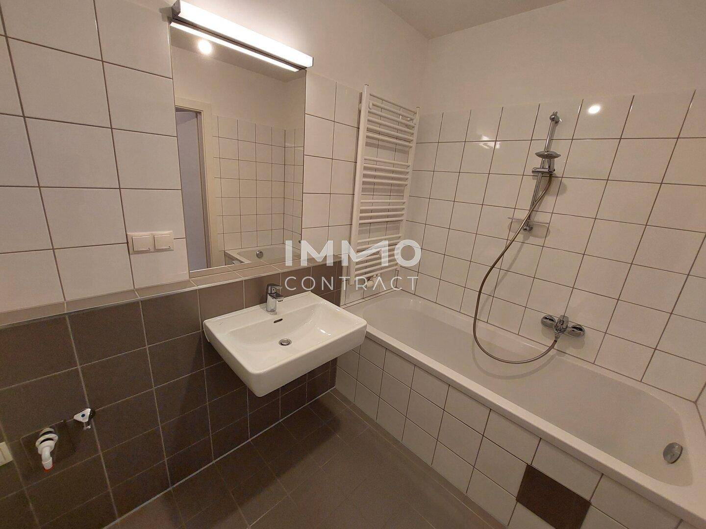 Badezimmer mit Badewanne, Waschbecken und Wandfliesen in Braun- und Weißtönen, inklusive Handtuchheizkörper.