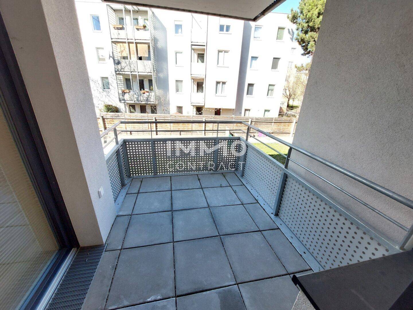 Geräumiger Balkon mit Fliesenboden und modernem Metallgeländer, Blick auf Nachbargebäude.