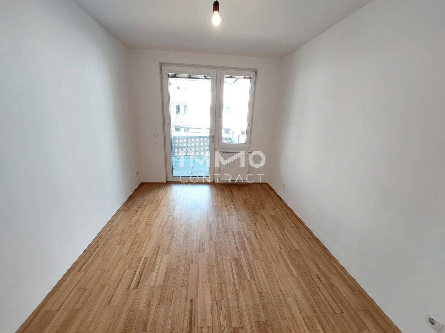 Leerer Raum mit Parkettboden und Zugang zu einem Balkon oder einer Terrasse, gut belichtet.