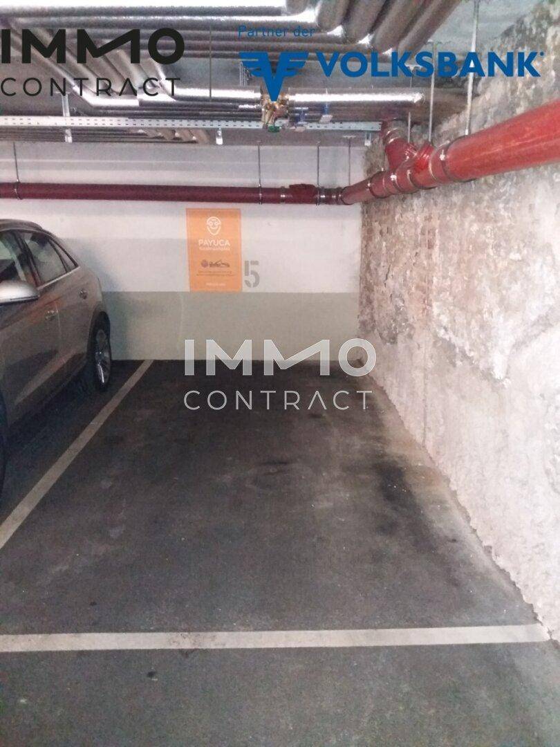 Tiefgaragenstellplatz mit robusten Betonwänden und roten Rohren an der Decke in einem Parkhaus.