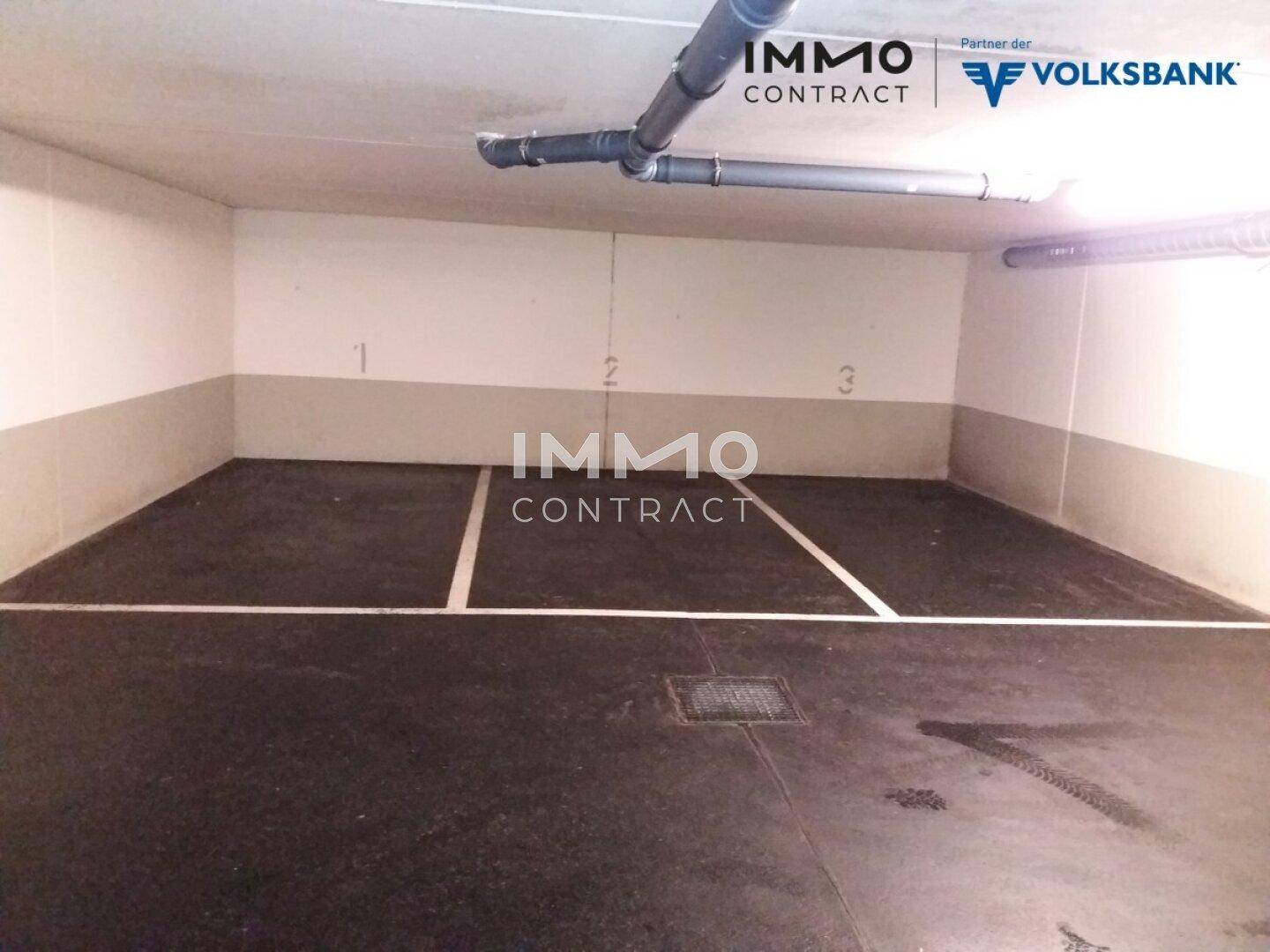 Tiefgarage mit markierten Stellplätzen und sichtbaren Versorgungsleitungen an der Decke.