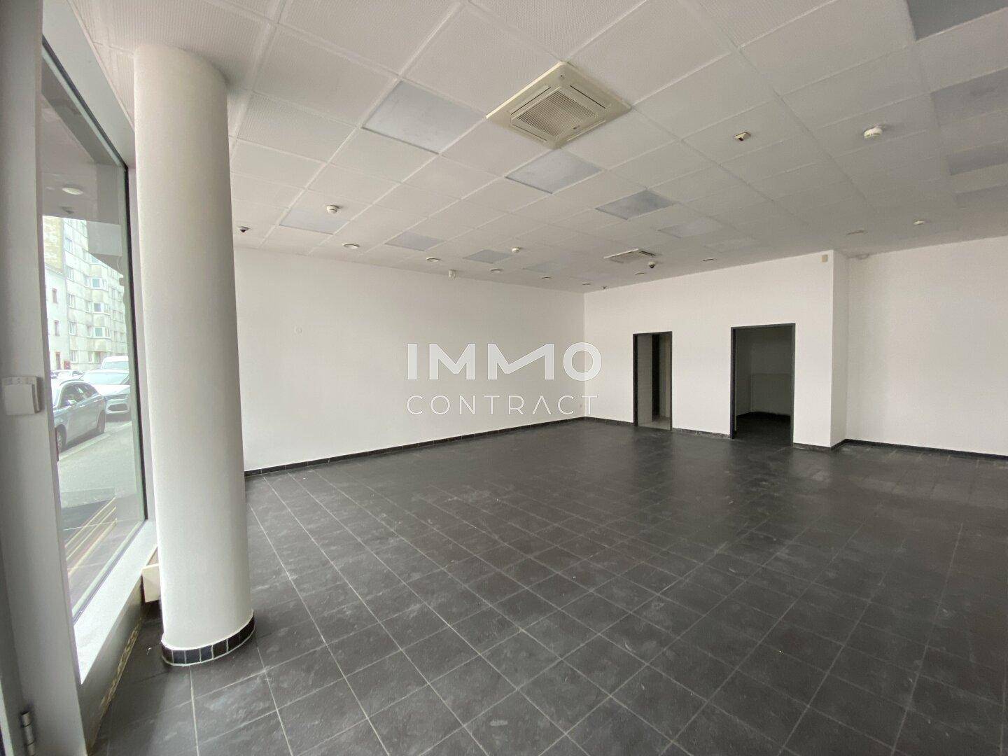 Offener Geschäftsraum mit Säule und Zugang zu weiteren Bereichen, ausgestattet mit dunklen Fliesen und großen Fenstern.