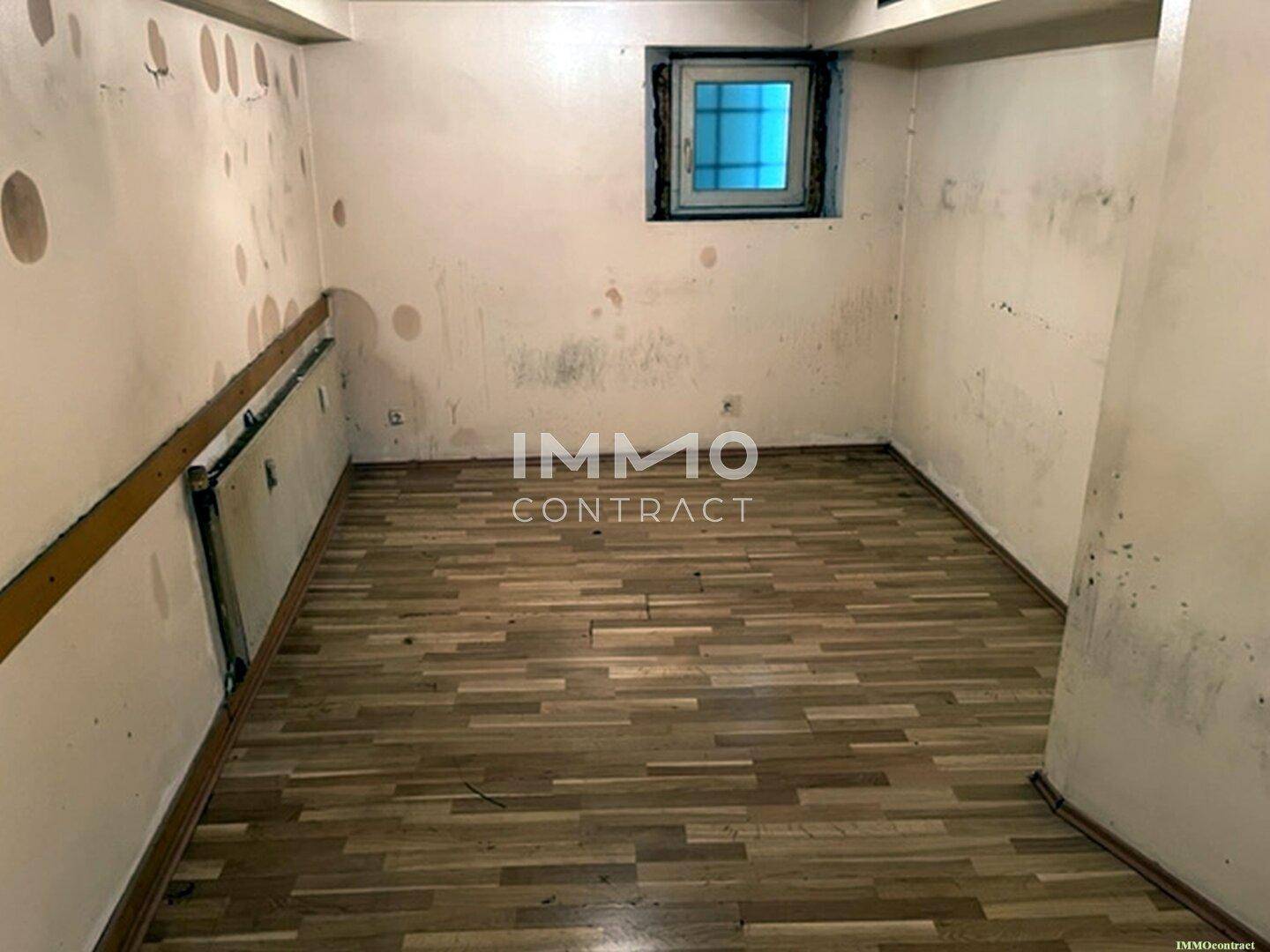 Einfacher Raum mit Laminatboden und einem kleinen Fenster, dessen Wände deutliche Gebrauchsspuren zeigen und renoviert werden müssen.