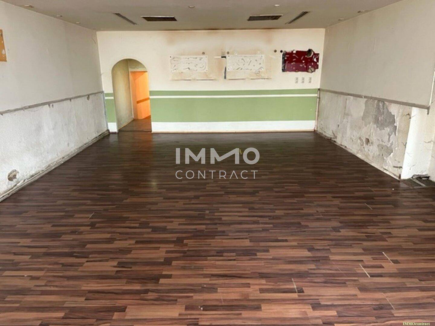 Langer, offener Ladenraum mit Laminatboden und teilweise beschädigten Wänden, der viel Potenzial für eine Neugestaltung bietet.