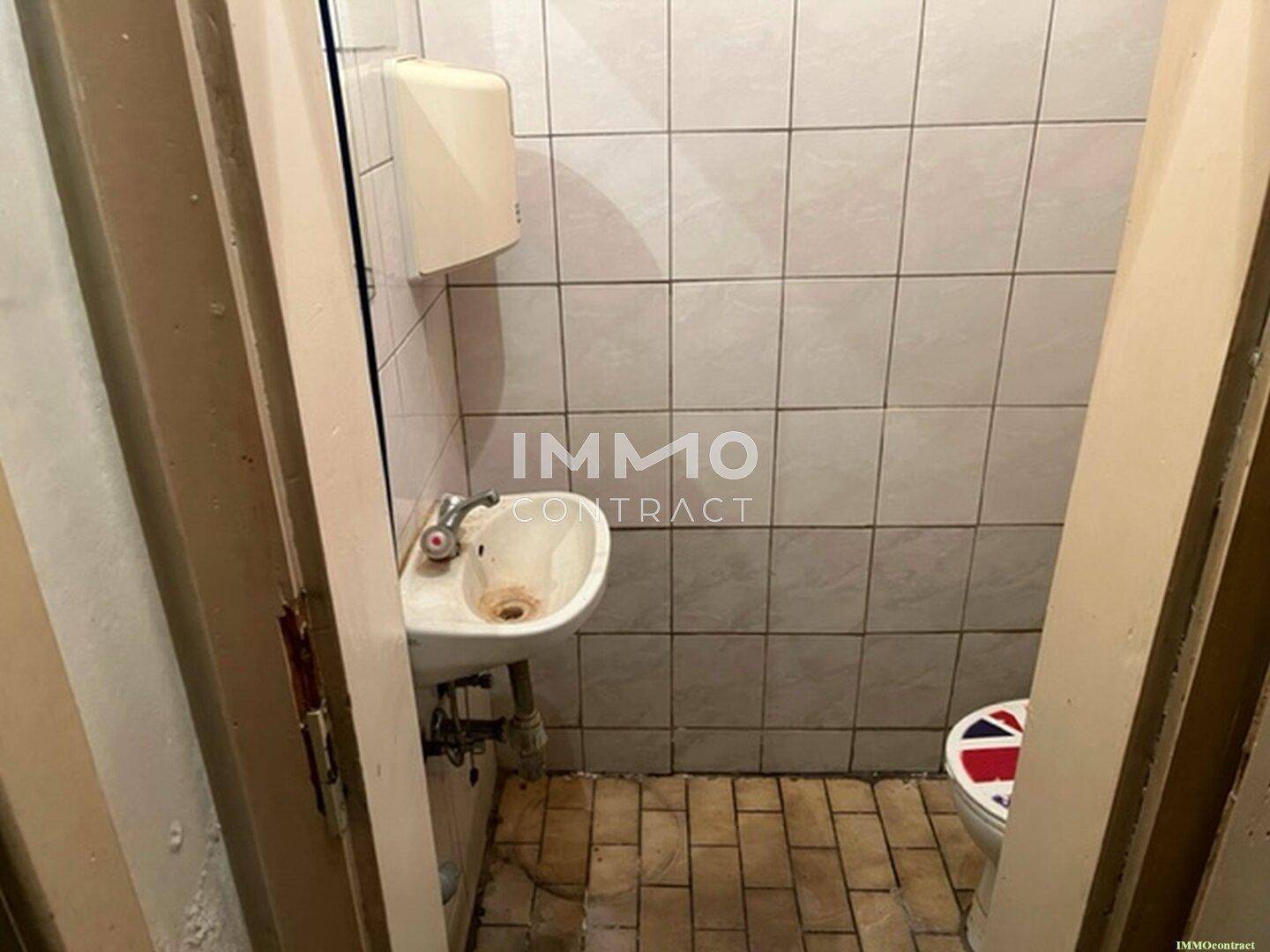 Kleine Toilette mit Fliesenboden, einem einfachen Waschbecken und Wandfliesen, die eine umfassende Renovierung benötigt.