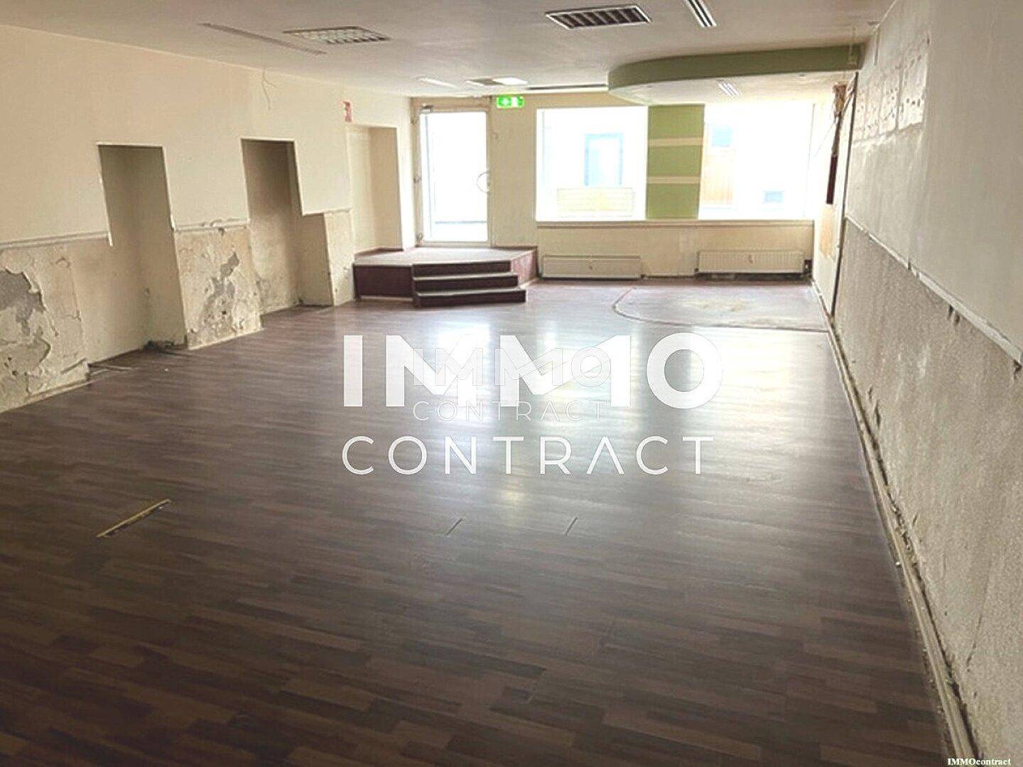 Geräumiger Ladenbereich mit dunklem Laminatboden und Wänden, die deutliche Abnutzungsspuren aufweisen und eine Renovierung erfordern.