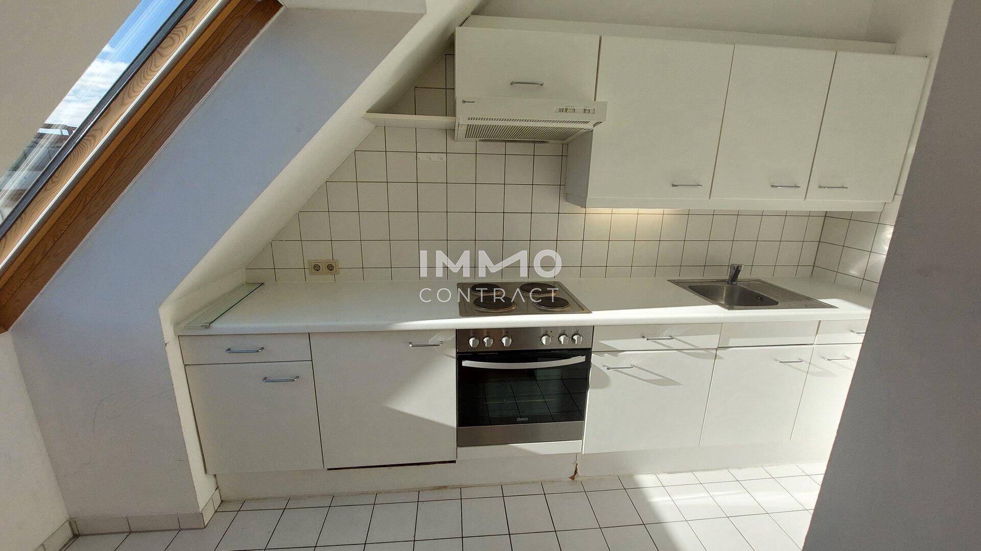 Kleine, funktionale Einbauküche unter einem Dachfenster mit weißen Schränken und Fliesenboden.