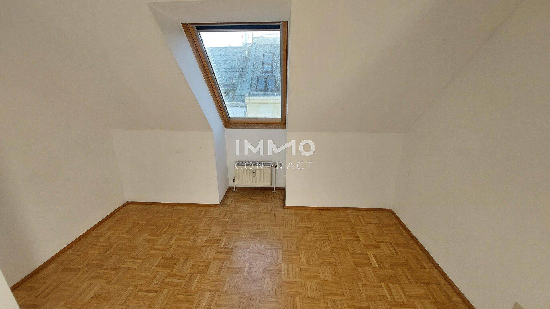 Gemütliches Dachzimmer mit Holzboden, einem großen Dachfenster und einem Heizkörper.