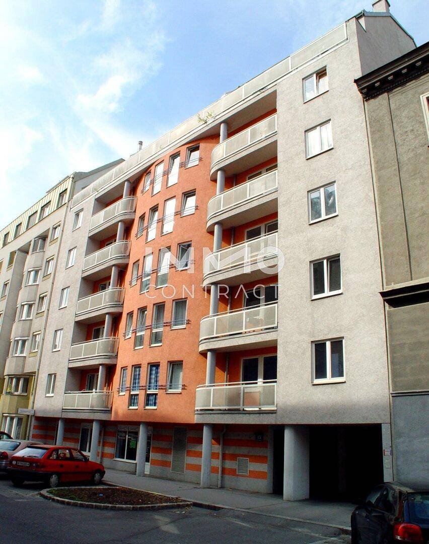 Ansicht der modernen Wohnhausfassade mit orangefarbenen Elementen, Balkonen und Parkplätzen.