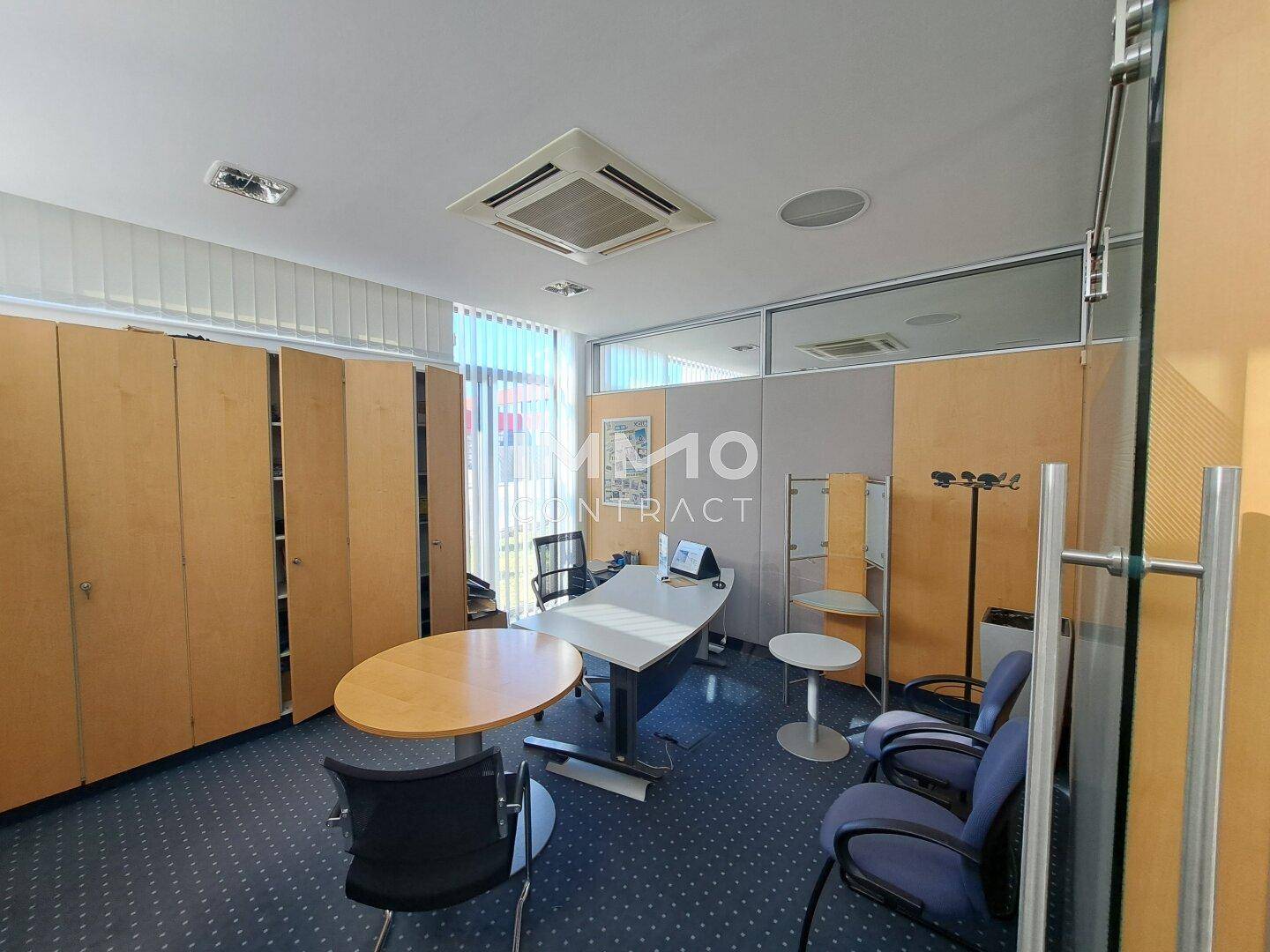 Modern eingerichtetes Büro mit Teppichboden, verstellbarem Schreibtisch und Besprechungsbereich.