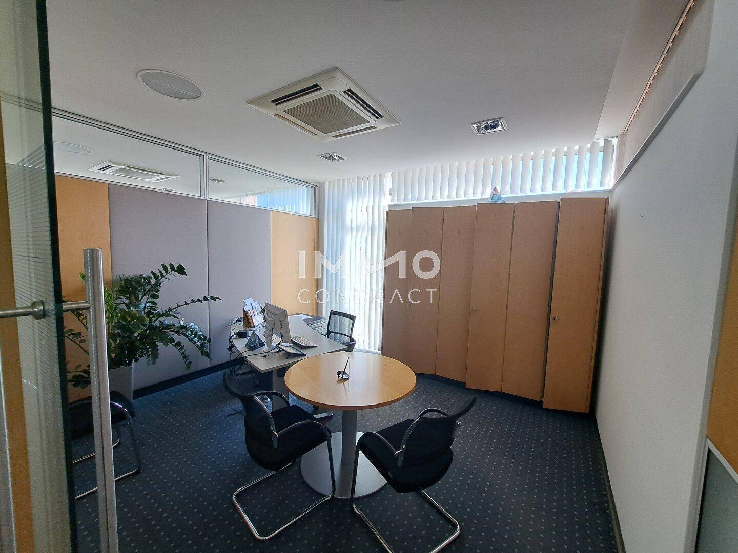 Abgetrenntes Büro oder Besprechungsraum mit Teppichboden, Holzeinbauschränken und einem runden Tisch.