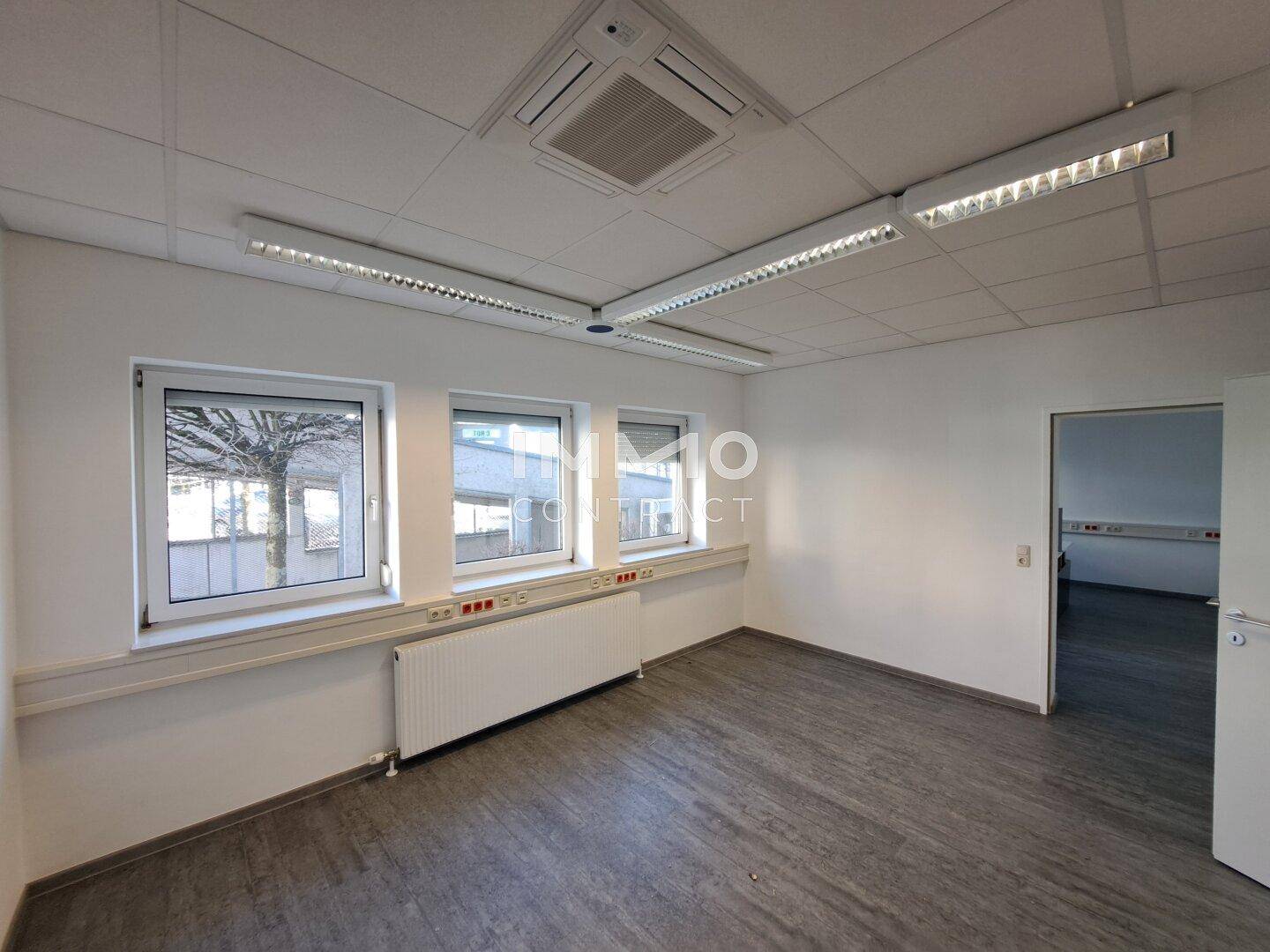 Geräumiges Büro mit drei Fenstern, Heizkörpern und Deckenbeleuchtung, bereit zur Einrichtung.