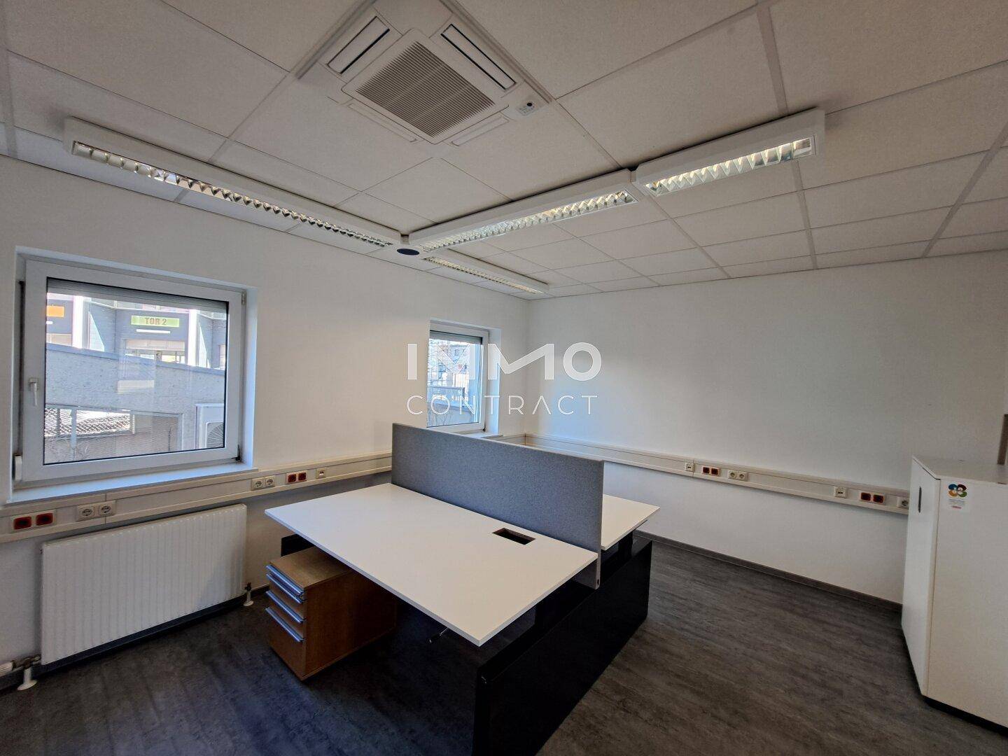 Helles Büro mit einem Arbeitsplatz, Fenstern und Deckenbeleuchtung, ideal für konzentriertes Arbeiten.