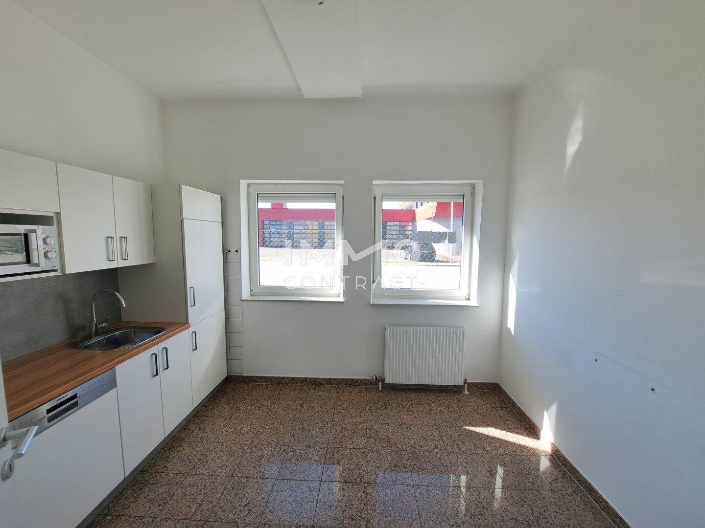 Kleine Küche mit weißen Schränken, Holzarbeitsplatte und Terrazzoboden, ideal für Pausen.