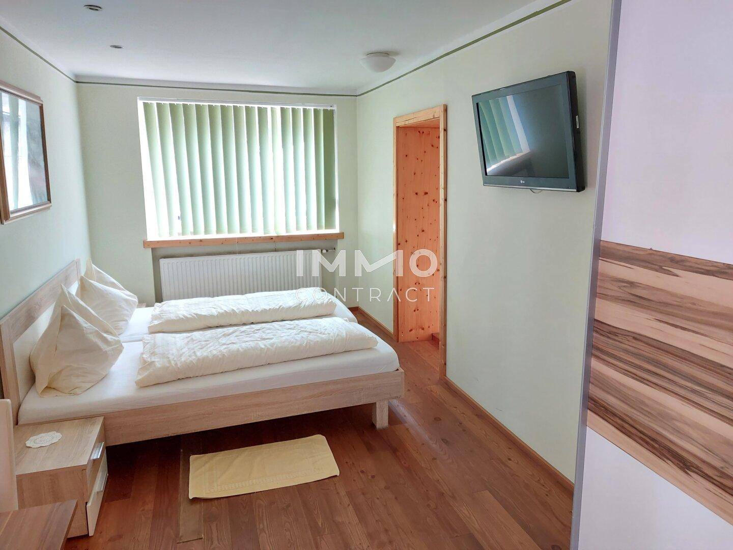 Gemütliches Schlafzimmer mit Holzbett, Parkettboden und einem an der Wand montierten Fernseher.