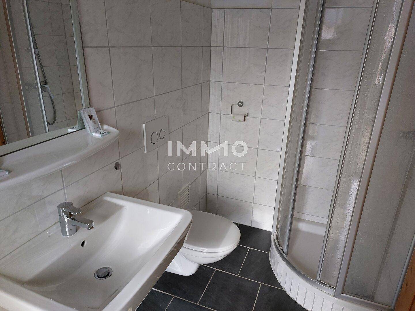 Funktionales Badezimmer mit weißen Wandfliesen, dunklem Boden und einer praktischen Eckdusche.