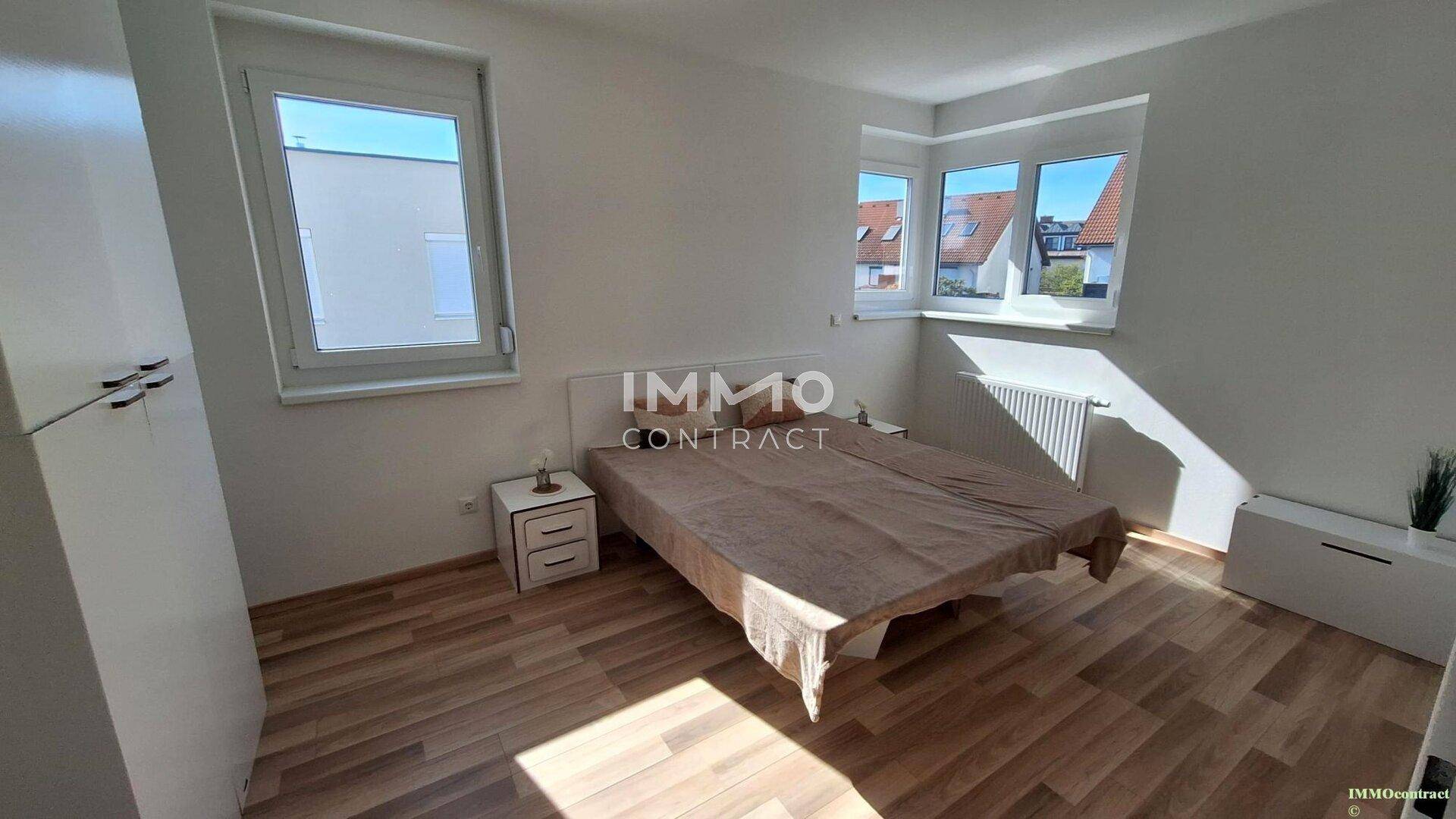 Schlafzimmer mit Doppelbett, Laminatboden und mehreren Fenstern für viel Licht.