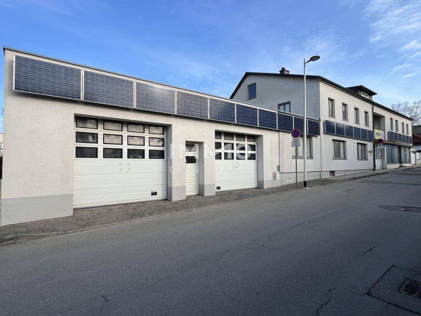 Rückansicht des Gebäudes mit Garagentoren und weiteren Solarpaneelen an der Fassade.