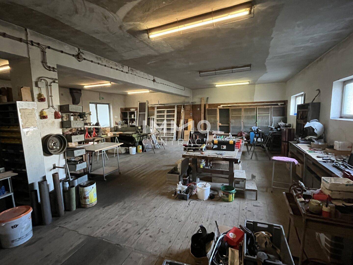 Großer Werkstattraum mit Holzboden, vielen Arbeitstischen und verschiedenen Geräten.