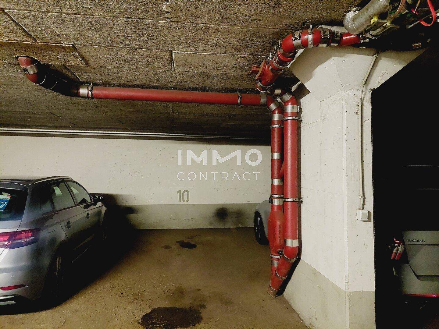 Sichtbare rote Rohrleitungen an der Decke der Tiefgarage über einem Parkplatz mit Nummerierung.