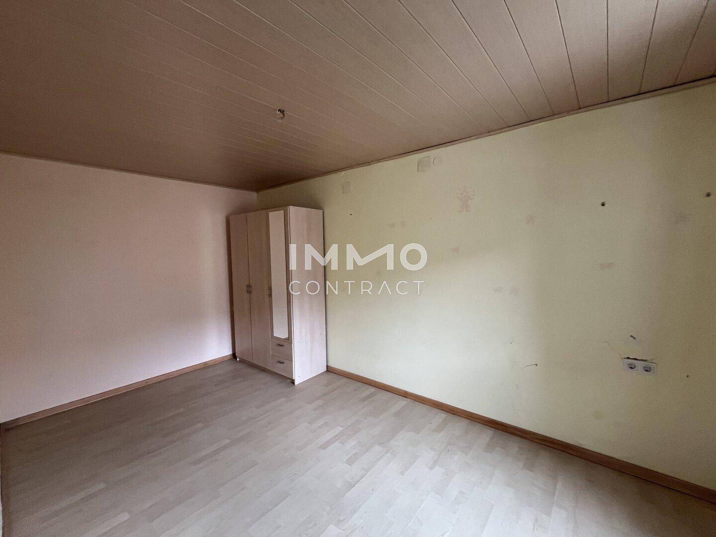 Leeres Schlafzimmer mit hellen Wänden, Laminatboden und einem kleinen Kleiderschrank.