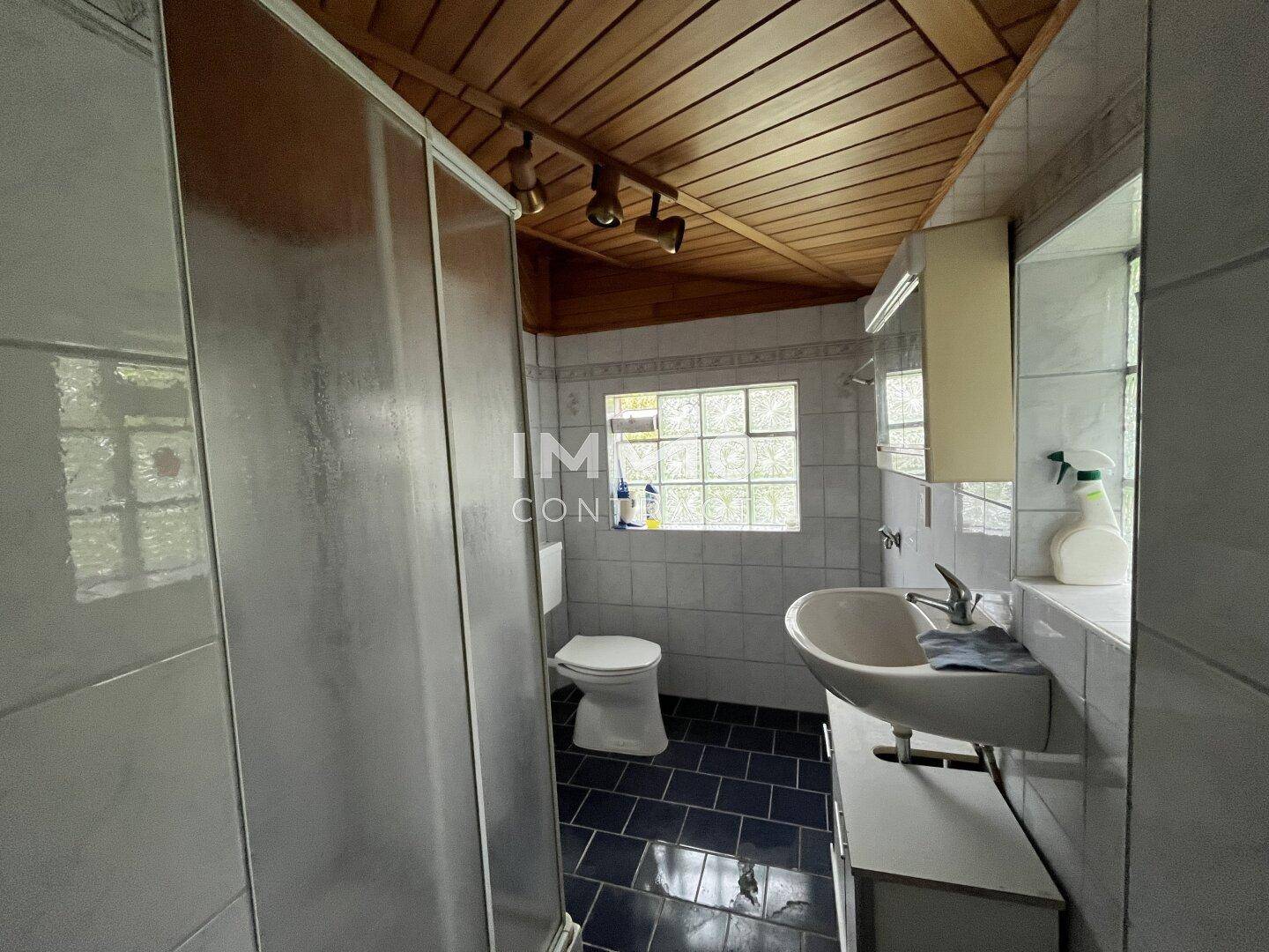 Badezimmer mit Duschkabine, Toilette und Waschbecken, ausgestattet mit Fliesen und Holzdecke.