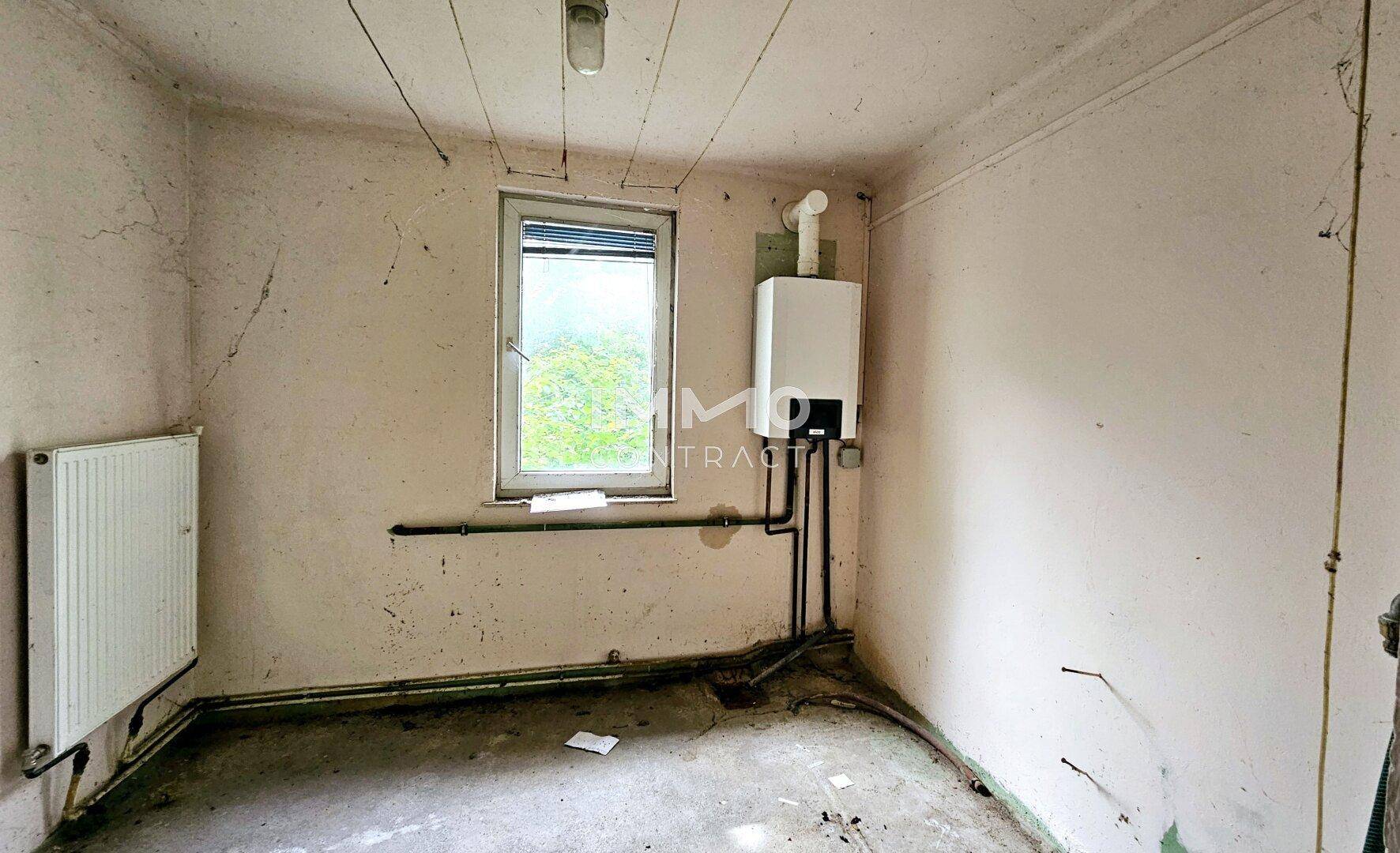 Kleiner Raum mit Heizungsanlage, Fenster und sichtbaren Rohren, der als Hauswirtschaftsraum dient.