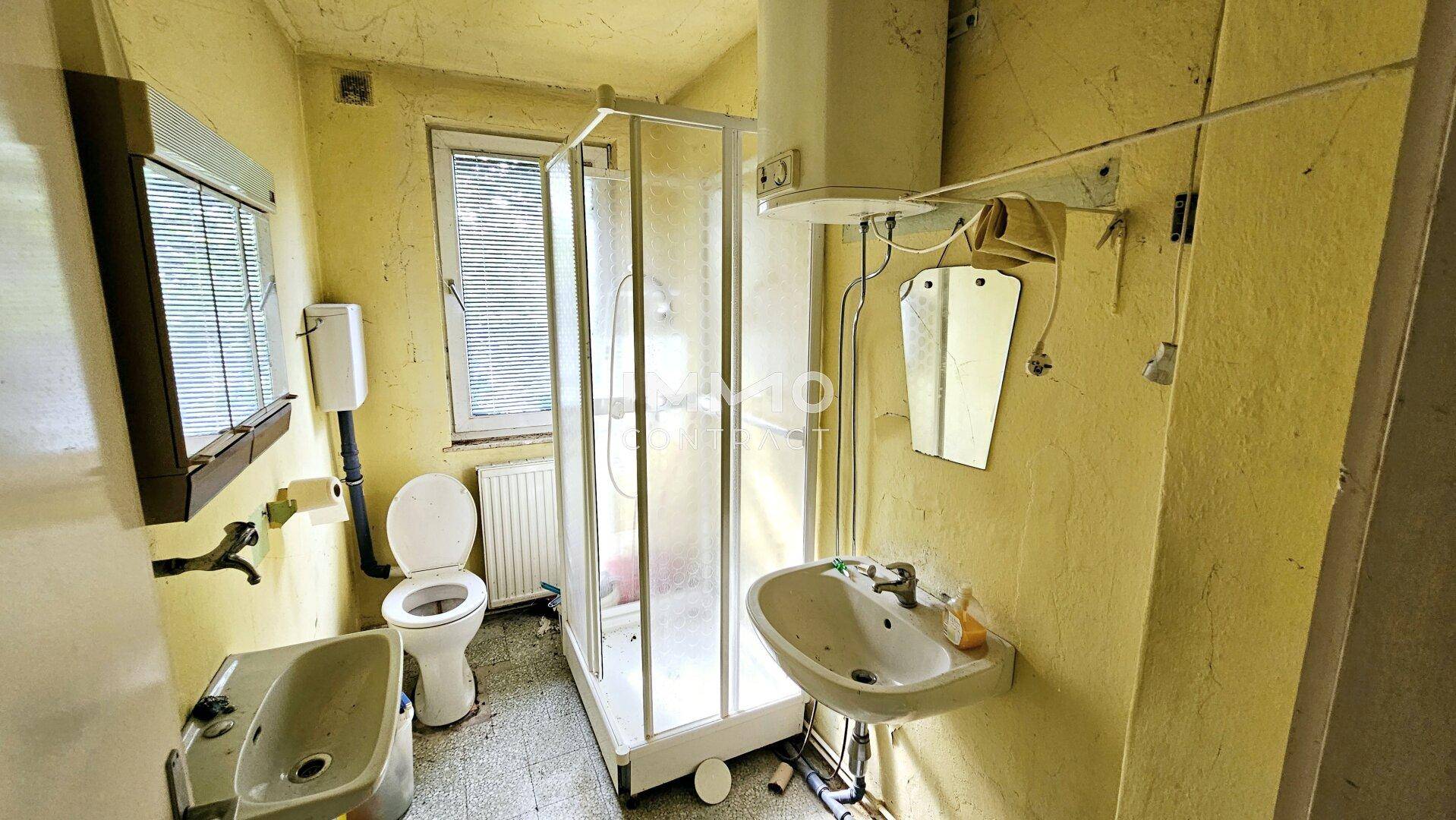 Veraltetes Badezimmer mit Dusche, Toilette, Waschbecken und Bidet in gelblichen Farbtönen.